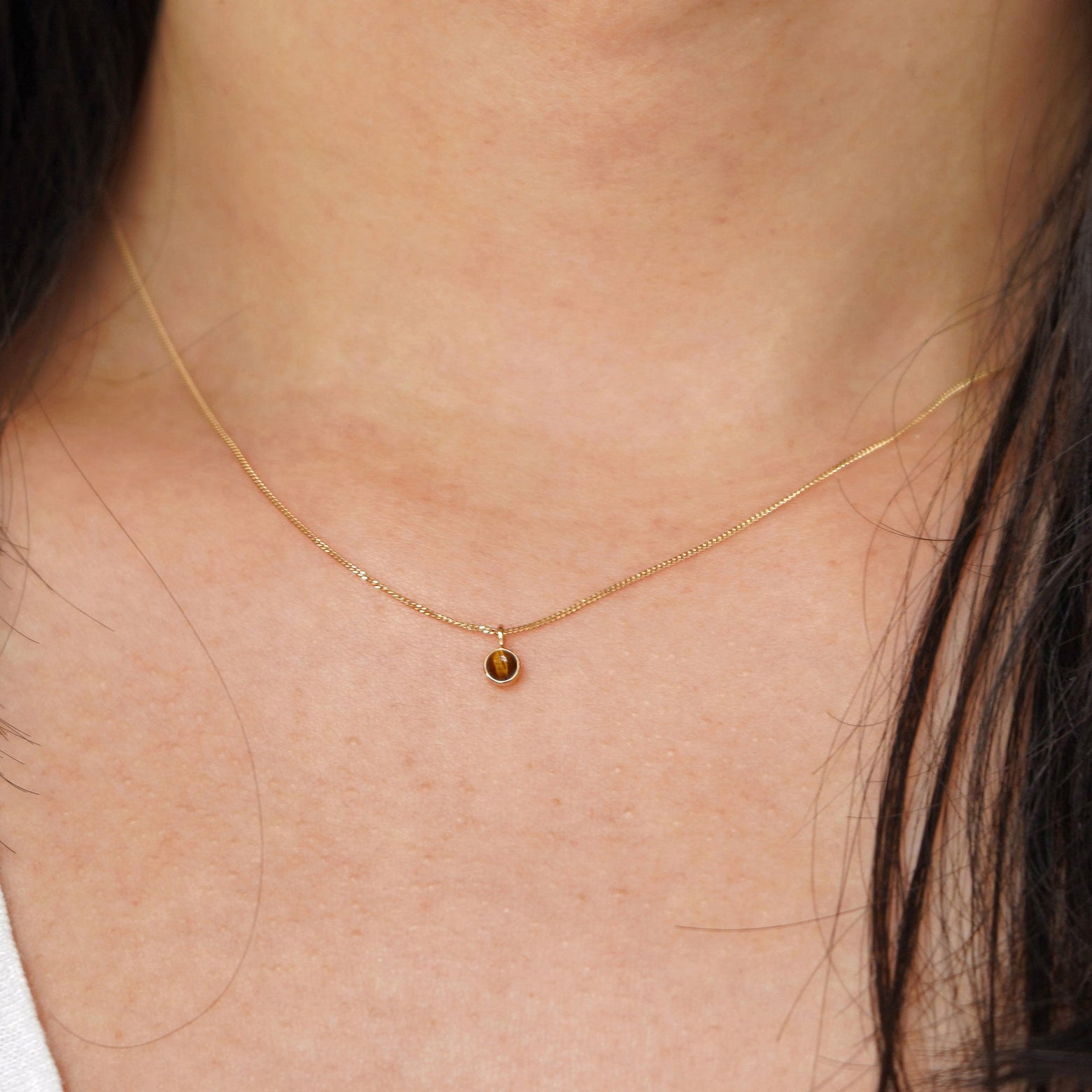 A model's neck wearing a solid 14k yellow gold Tiger Eye necklace