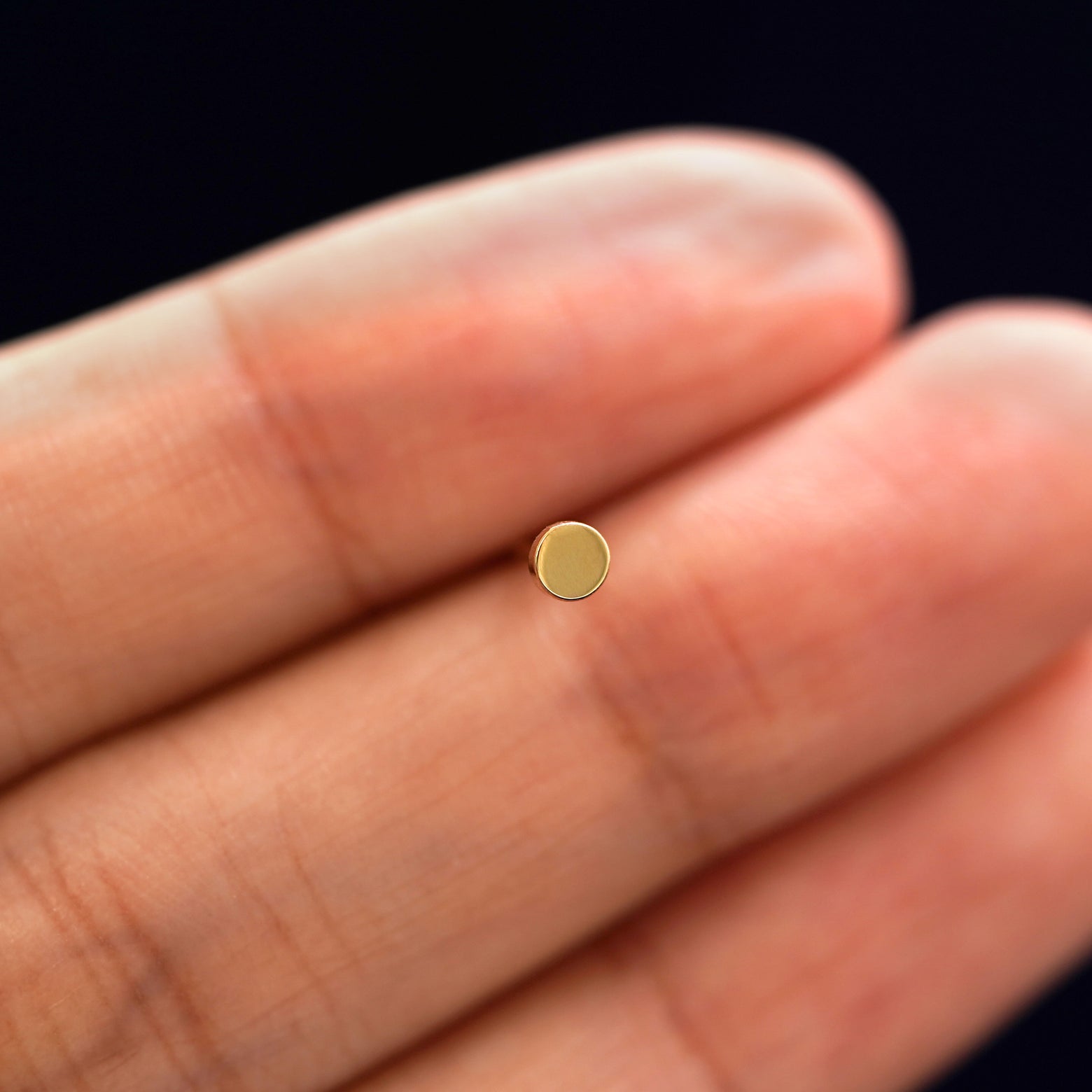 A solid 14k yellow gold Small Circle Earring in between a model's fingers