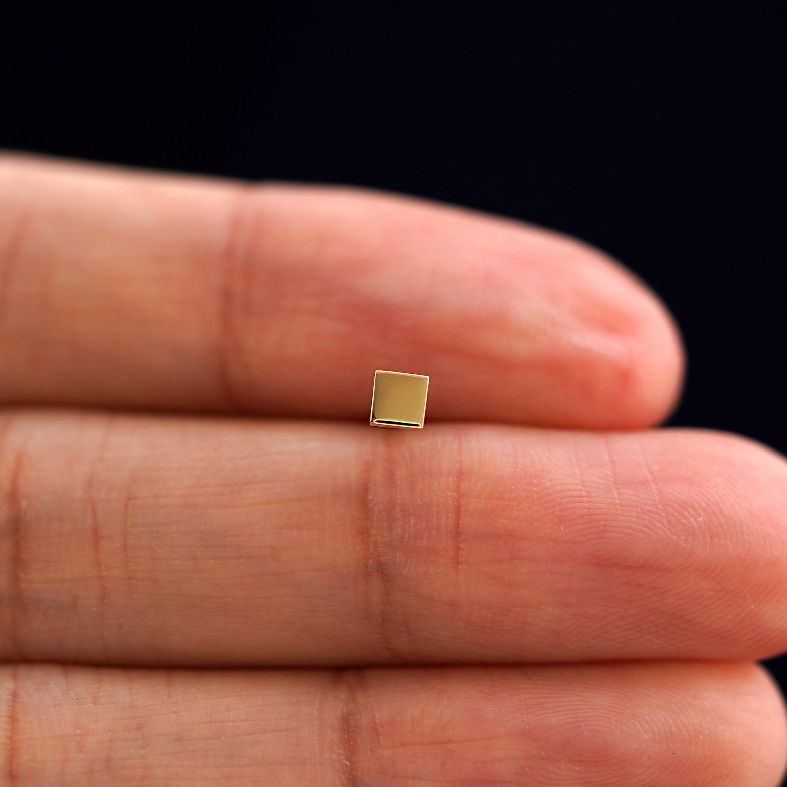 A solid 14k yellow gold Square Earring in between a model's fingers