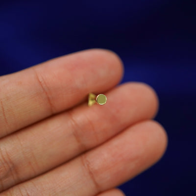 A solid yellow gold Triangle Flatback Piercing laying facedown on a model's finger to show the end of the flat back