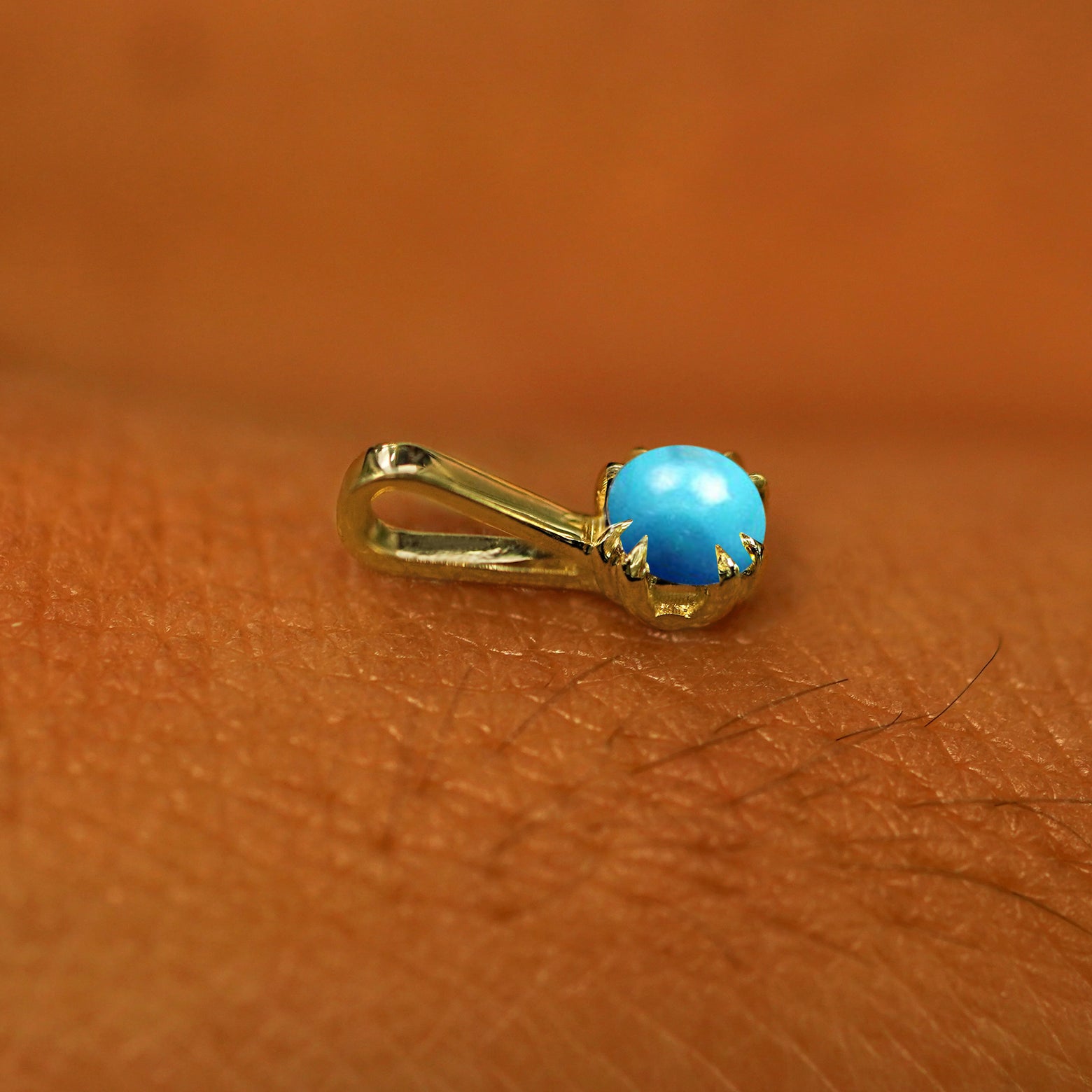 A 14k yellow gold Turquoise Charm for chain resting on the back of a model's hand