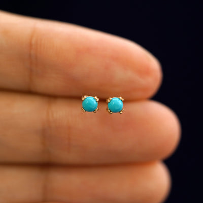 A model holding a pair of solid yellow gold turquoise 3mm Gemstone Earrings between their fingers