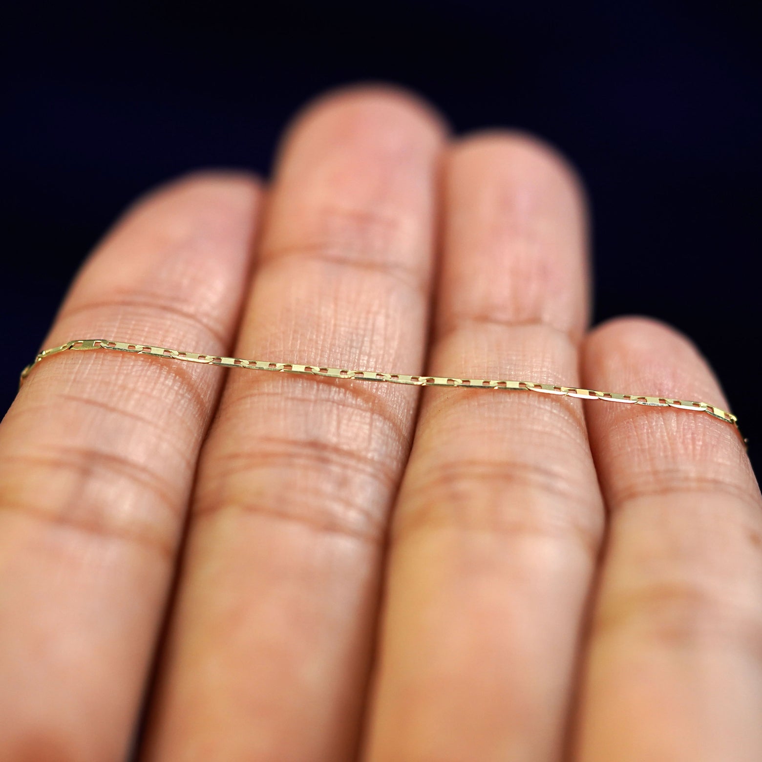 A yellow gold Valentine Bracelet resting on a model's fingers