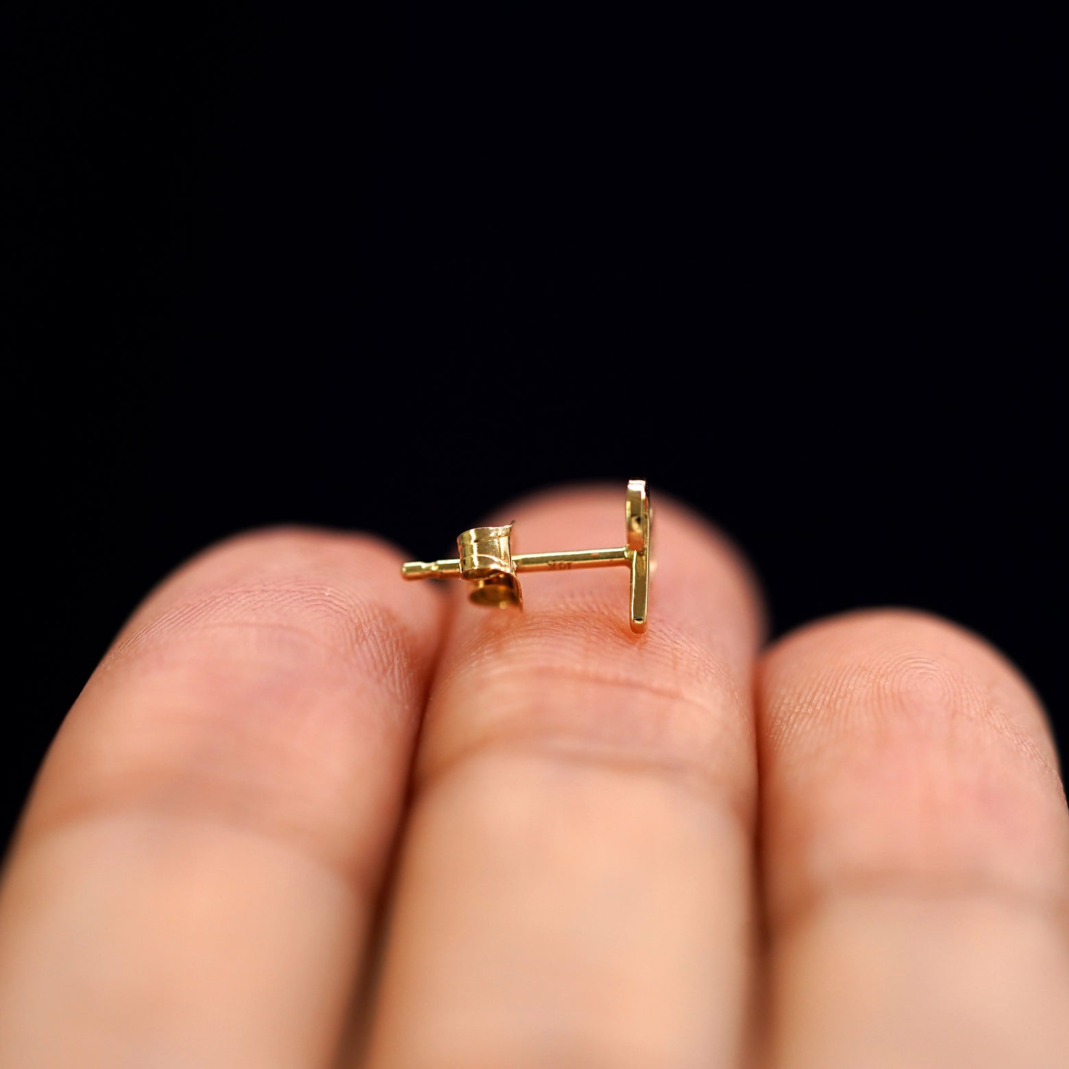A 14k gold Aries Horoscope Earring sitting sideways on a model's fingertips to show detail