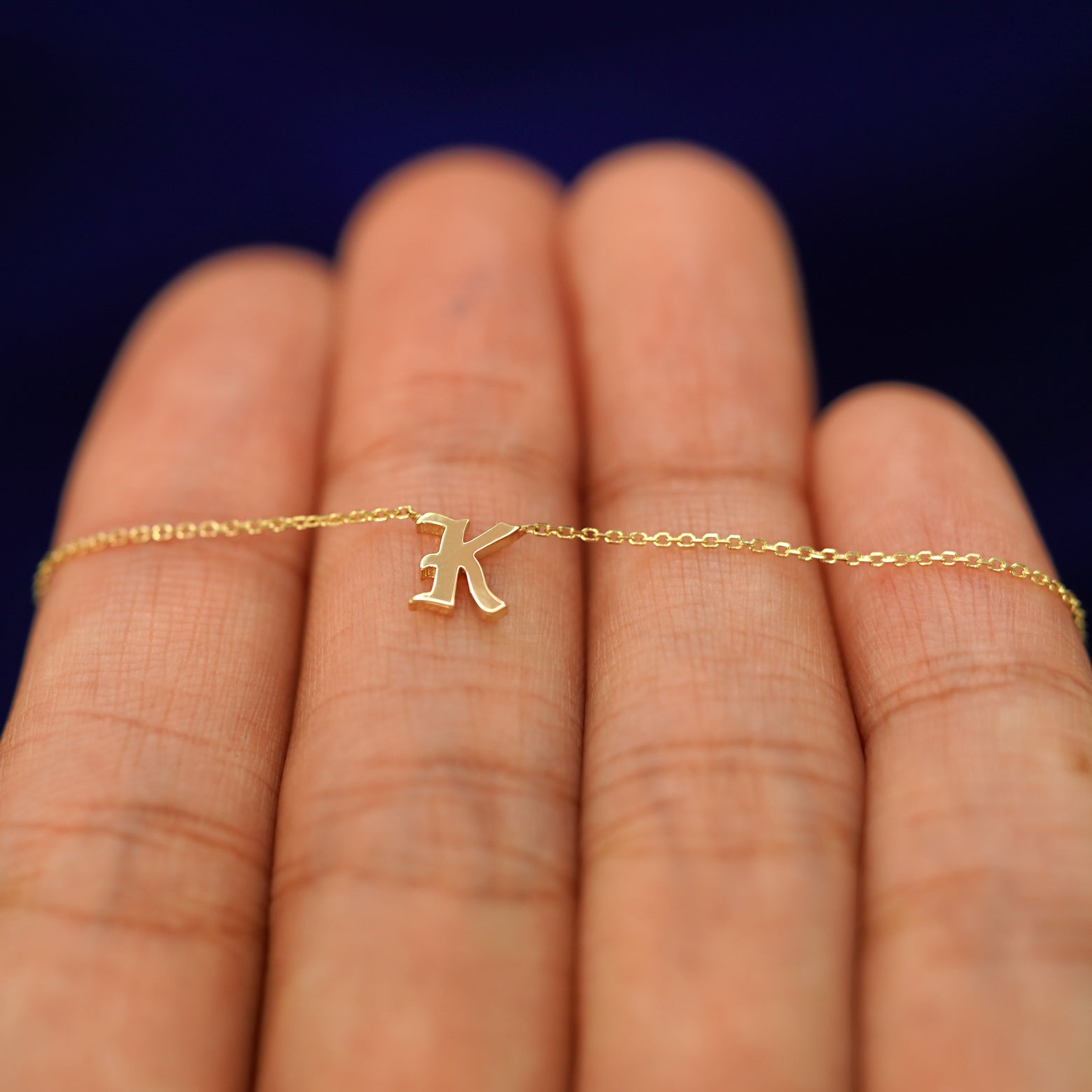 Close up view of a model's hand holding a yellow gold Initial Necklace with the letter K