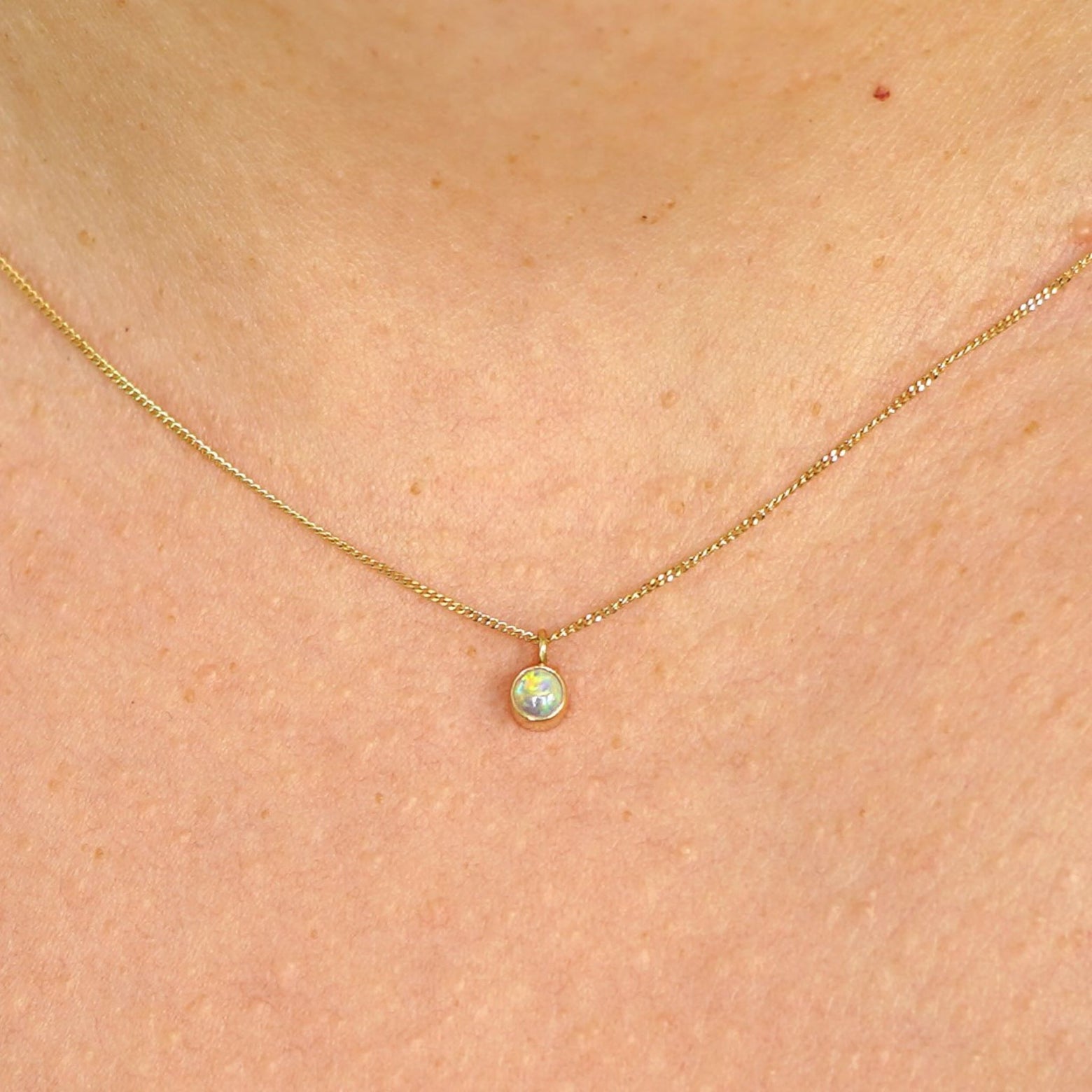 Close up view of a model's neck wearing a solid 14k yellow gold Opal necklace