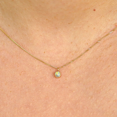 Close up view of a model's neck wearing a solid 14k yellow gold Opal necklace