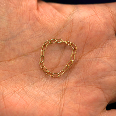 A solid yellow gold Veren Ring sitting in a model's palm to show thickness of the chain