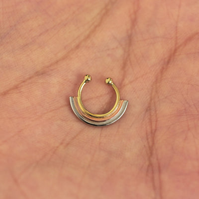 A model's hand holding a 14 karat yellow gold Non-Pierced Rainbow Septum