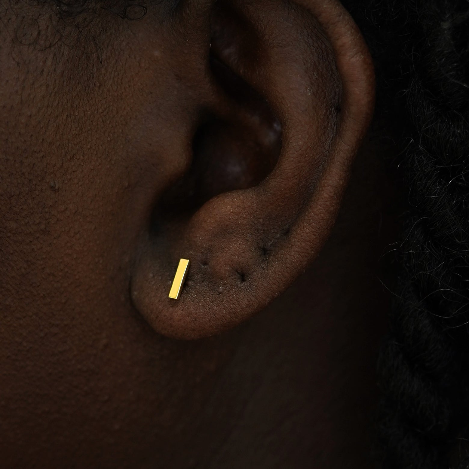 Close up view of a model's ear wearing a 14k yellow gold Bar Earring