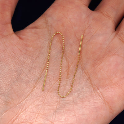 A solid 14k yellow gold Threader sitting in a model's palm with the beaded chain in a wave to show its flexibility