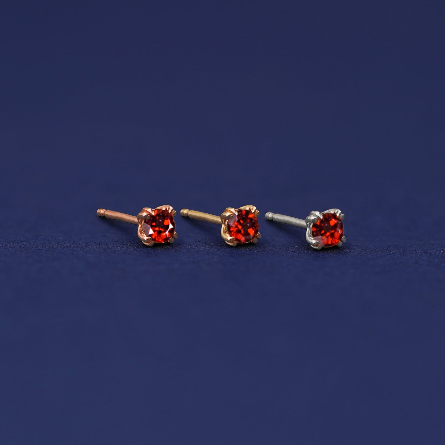 Three versions of the Garnet Earring shown in options of rose, yellow, and white gold