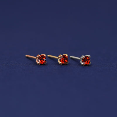 Three versions of the Garnet Earring shown in options of rose, yellow, and white gold