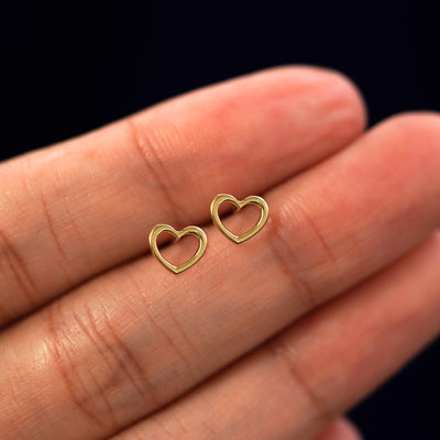 A model's hand holding a pair of recycled 14k gold Heart Earrings