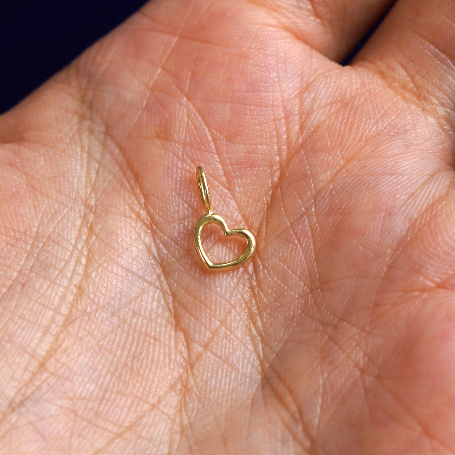 A solid gold Heart Charm for chain resting in a model's palm