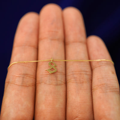 Close up view of a model's hand holding a yellow gold Initial Charm Necklace with the letter S