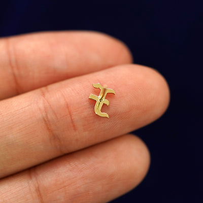 A solid 14k gold Initial Earring in the letter F laying face down on a model's fingertip to show the underside of the initial