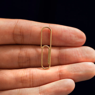 A solid 14k gold Not A Paper Clip Earring resting on a model's fingers