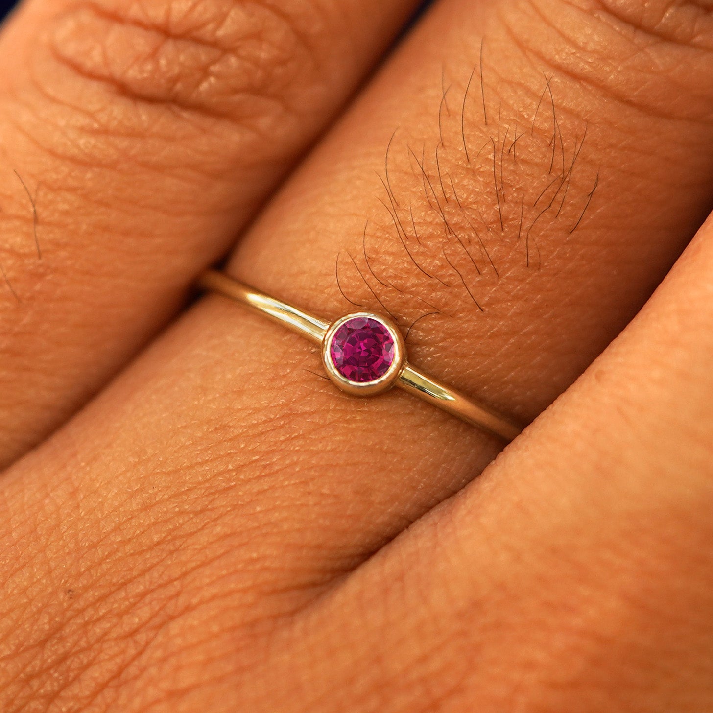 Close up view of a model's hand wearing a yellow gold Ruby Ring