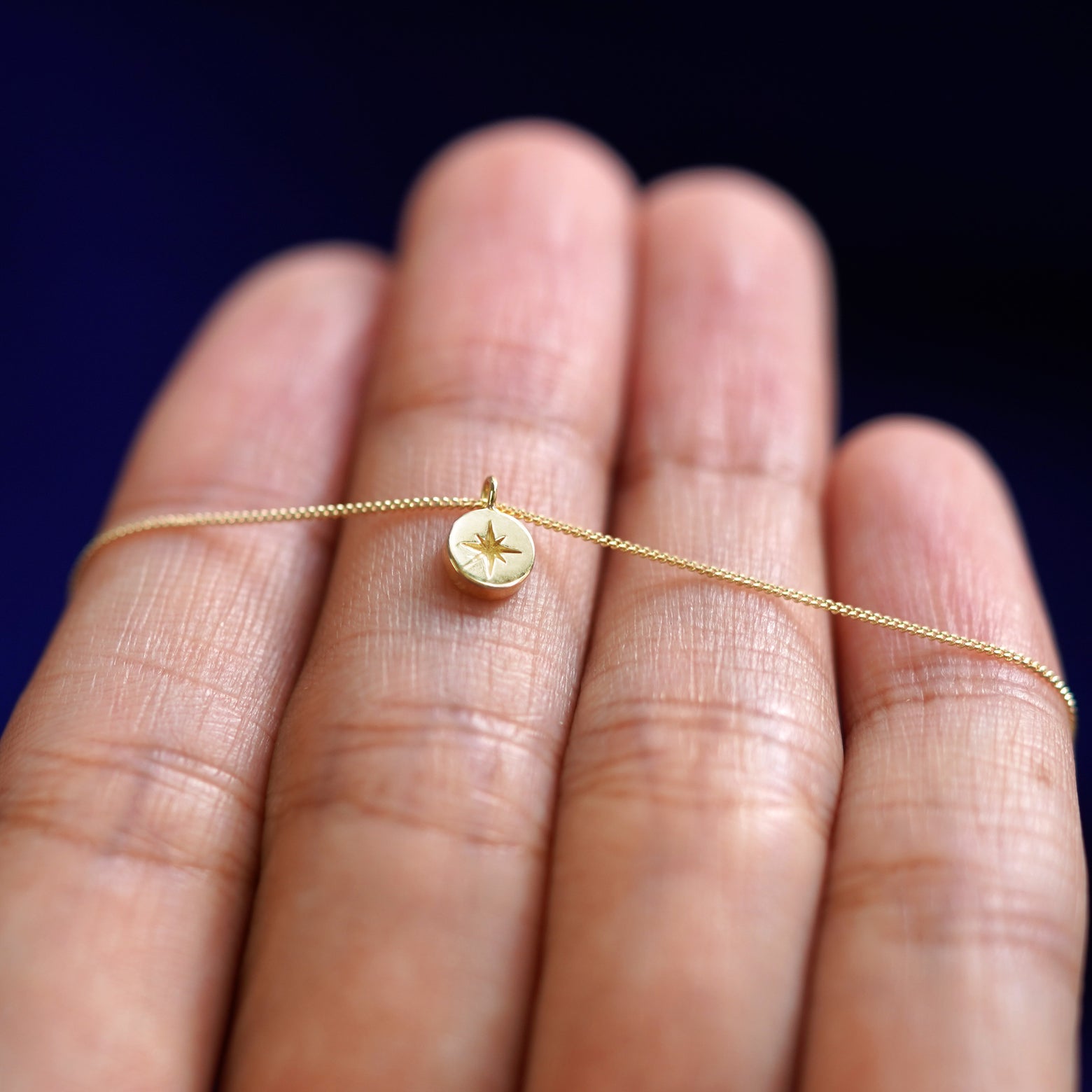 A yellow gold Star Disk Necklace resting on a model's fingers