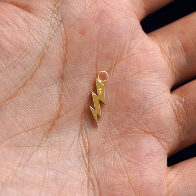 A 14k gold Lightning Bolt Charm for earring resting in a model's palm to show the underside of the charm