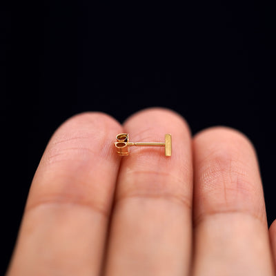 A 14k gold Triangle Earring sitting sideways on a model's fingertips to show detail