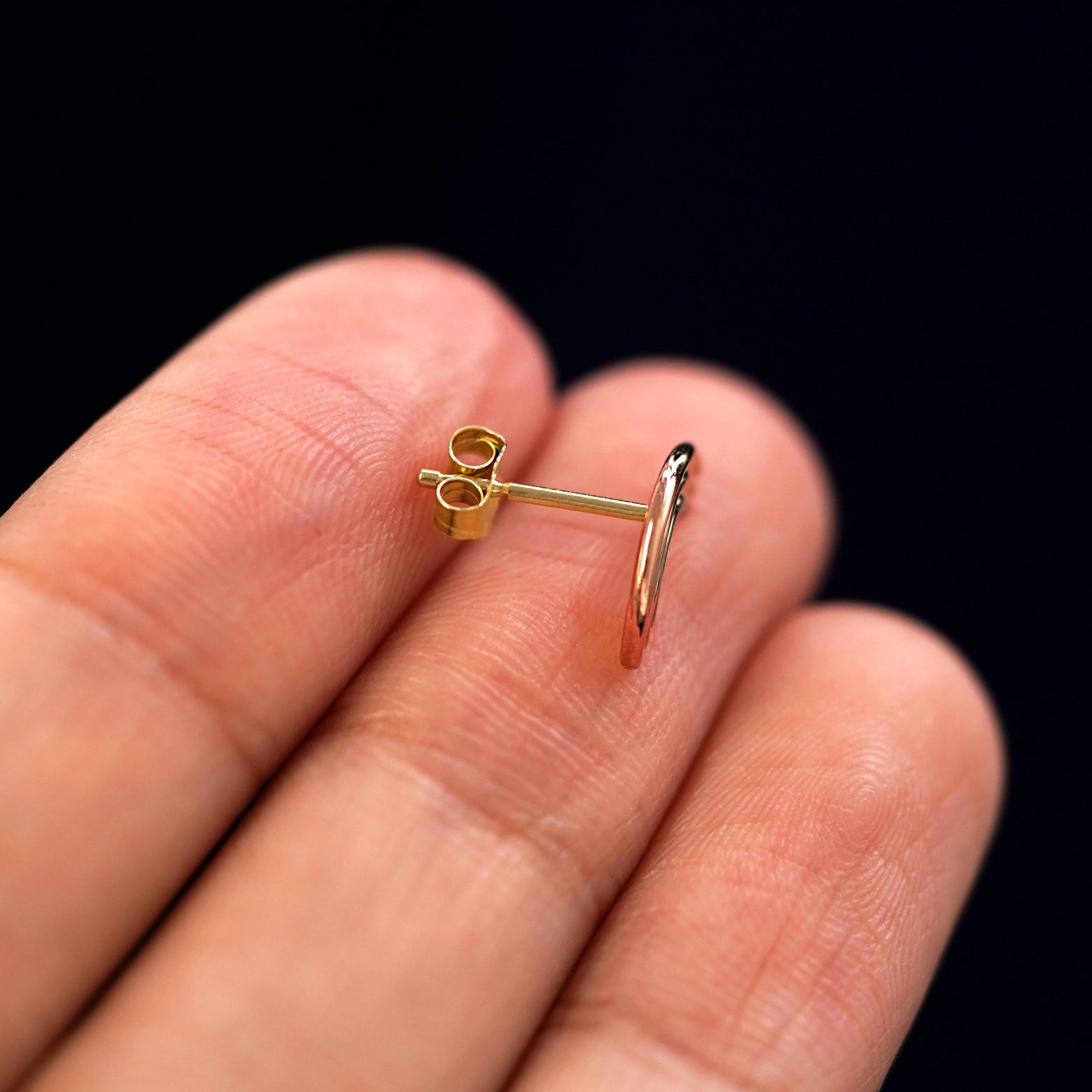 A 14k gold Rainbow Earring sitting sideways on a model's fingertips to show detail