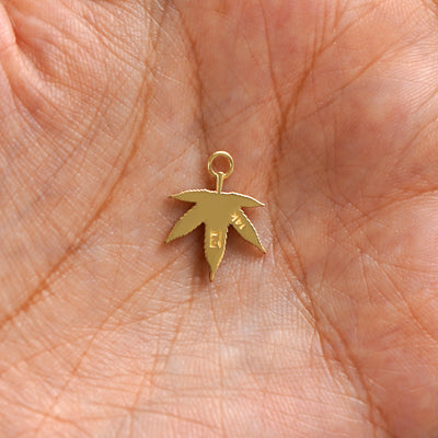A 14k gold Cannabis Charm for earring resting in a model's palm to show the back of the charm