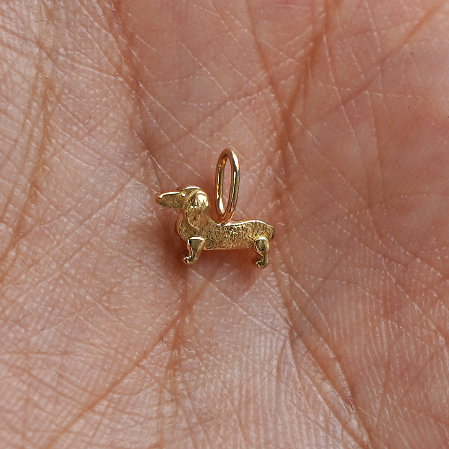 A solid gold Dog Charm for chain resting in a model's palm