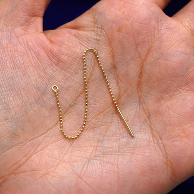 A solid 14k yellow gold Extender sitting in a model's palm with the beaded chain in a arch to show its flexibility