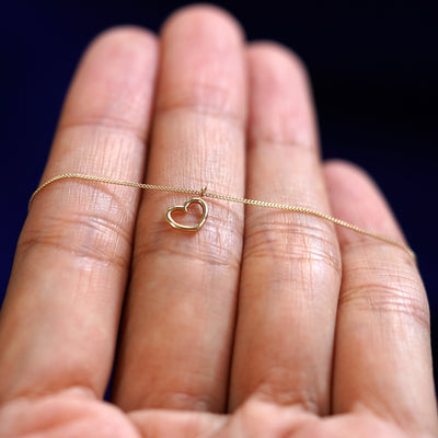 A yellow gold Heart Necklace resting on a model's fingers