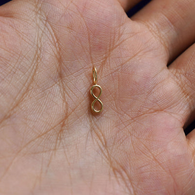 A solid gold Infinity Charm for chain resting in a model's palm