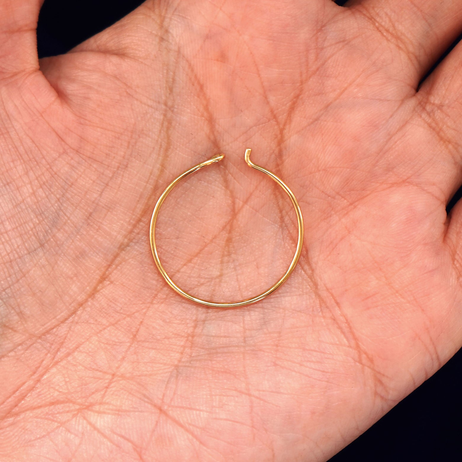 A solid 14k yellow gold Medium Hoop Earring open in a model's palm to show the easy hook closure