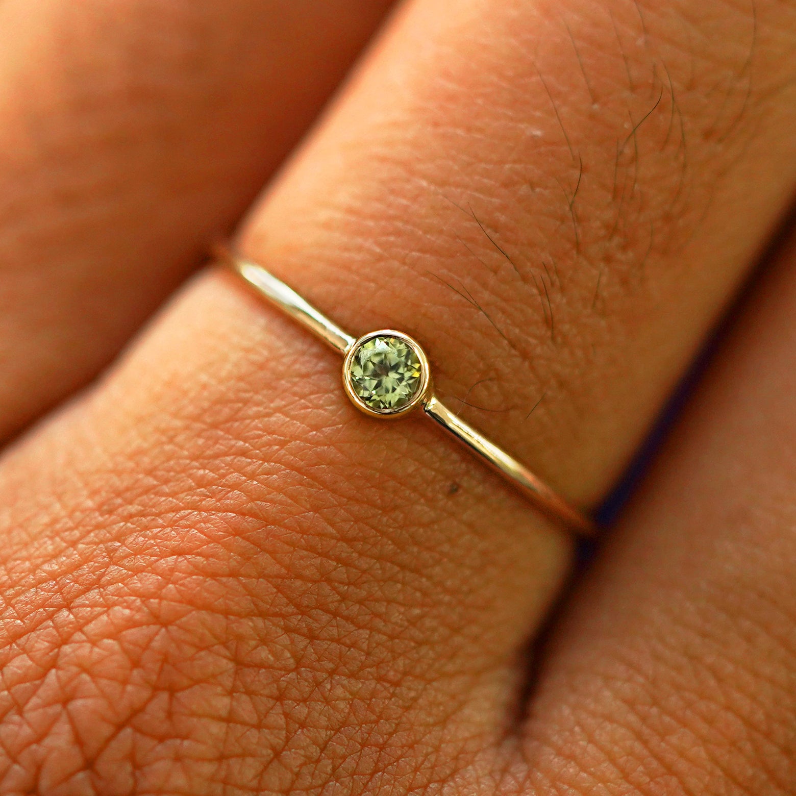 Close up view of a model's fingers wearing a solid yellow gold gemstone Peridot Ring