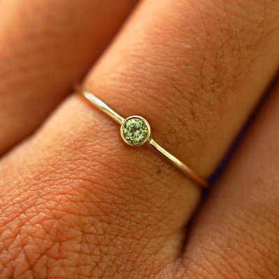 Close up view of a model's fingers wearing a solid yellow gold gemstone Peridot Ring