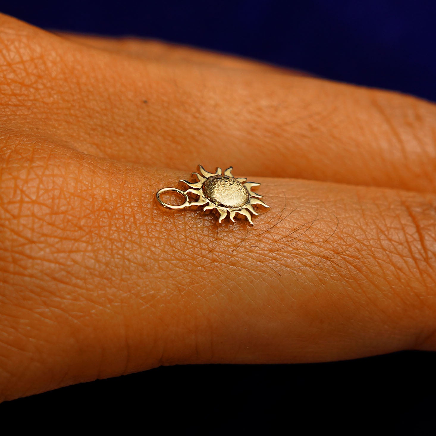 A 14k yellow gold Sun Charm for earring balancing on the back of a model's finger