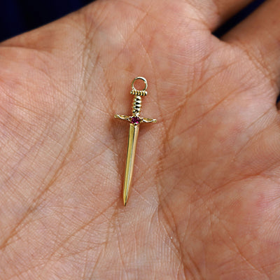 A solid gold ruby Sword Charm for earring resting in a model's palm