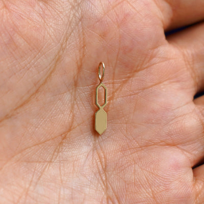 A solid gold Tanlah Charm for chain resting in a model's palm