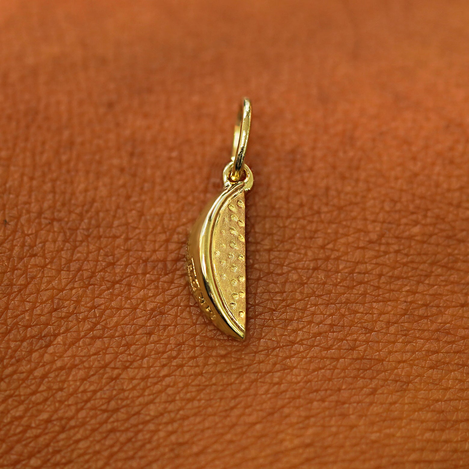 A solid 14k yellow gold Watermelon Charm resting on the back of a model's hand