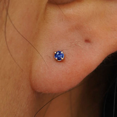 Close up view of a model's ear wearing a 14k yellow gold 2mm Blue Sapphire Gemstone Earring