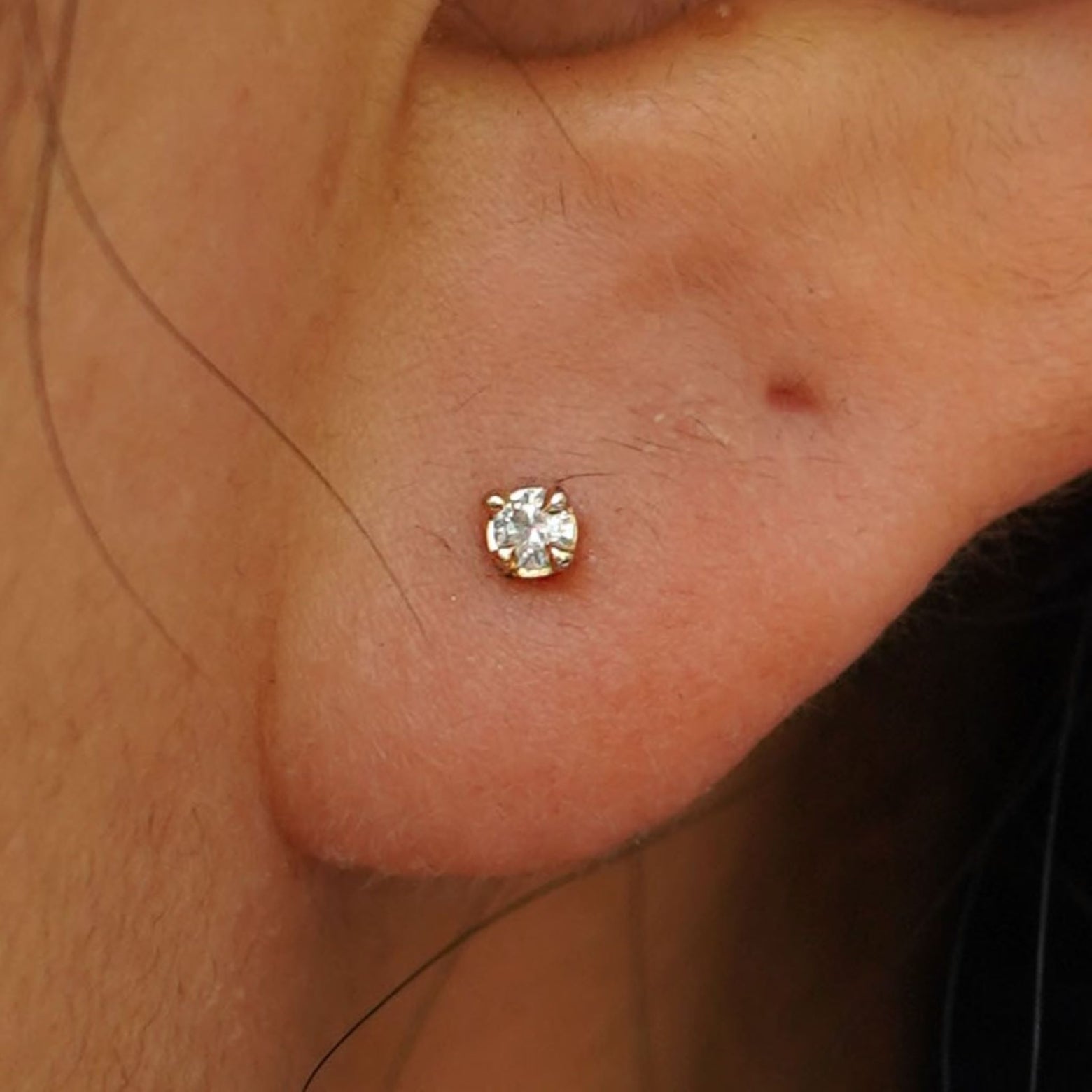 Close up view of a model's ear wearing a solid 14k yellow gold 2mm White Diamond Earring