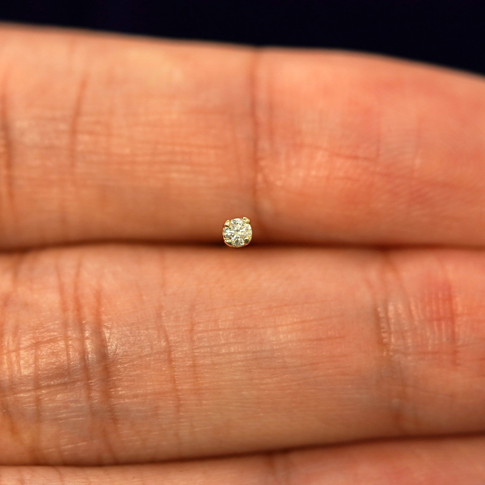 A yellow gold 2mm Diamond Earring in between a models fingers