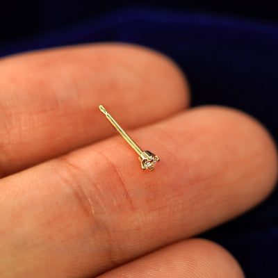 A yellow gold 2mm Diamond Earrings resting on a models fingertip