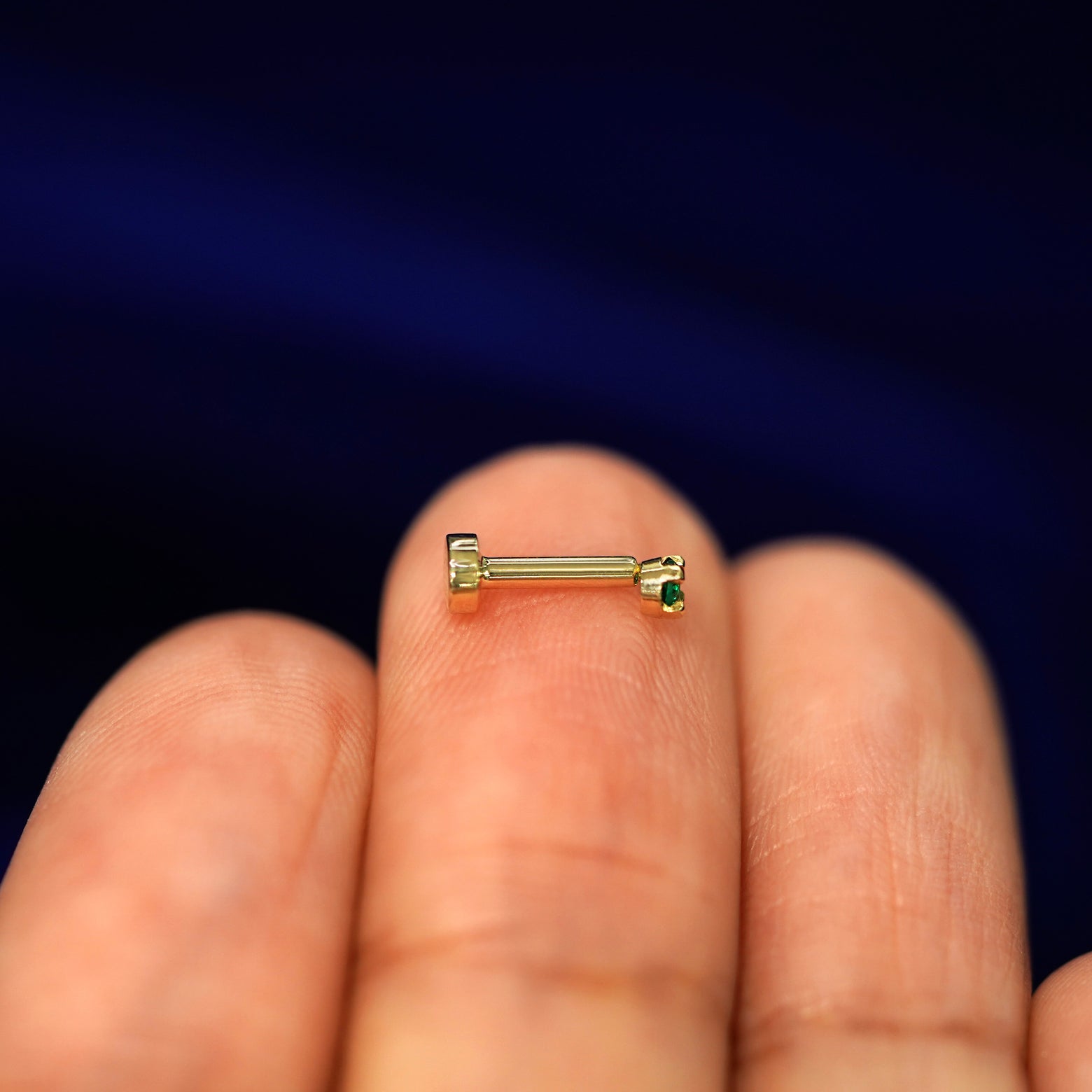 Side view of a yellow gold 2mm Emerald Gemstone Flatback Piercing on a model's fingertips