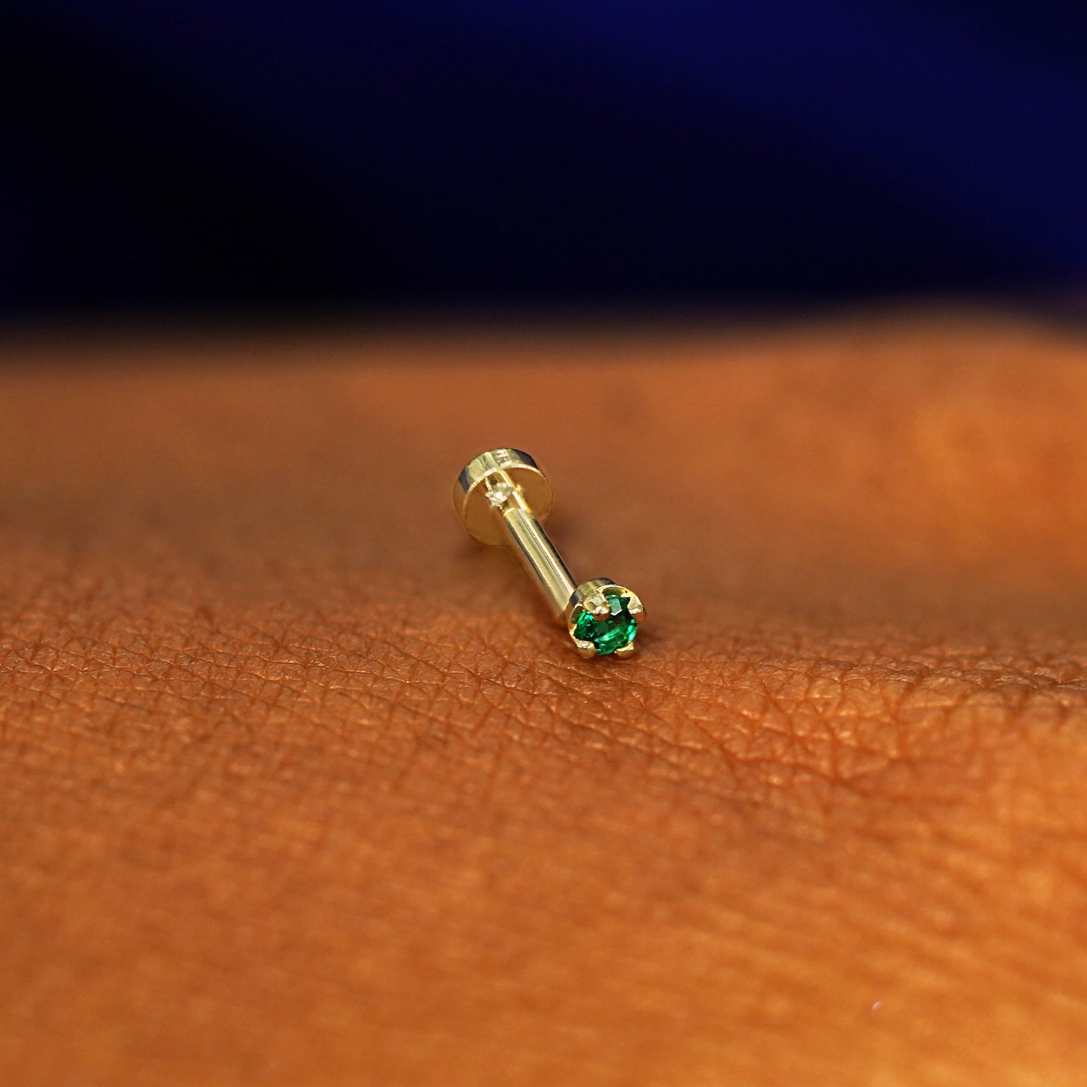 A solid 14k yellow gold 2mm Emerald Gemstone Flatback Piercing resting on the back of a model's hand