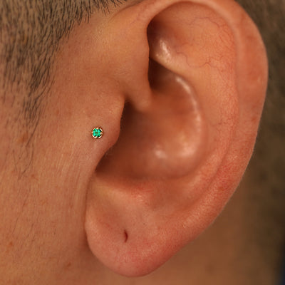 A model's ear wearing a 14k yellow gold 2mm emerald Gemstone Flatback in a tragus piercing