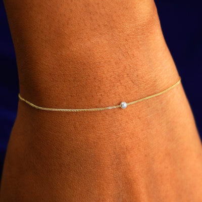 A model's wrist wearing a yellow gold Pearl Slide Bracelet with a 2mm pearl