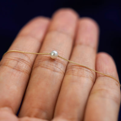 A 4mm pearl slide necklace resting on a model's fingers