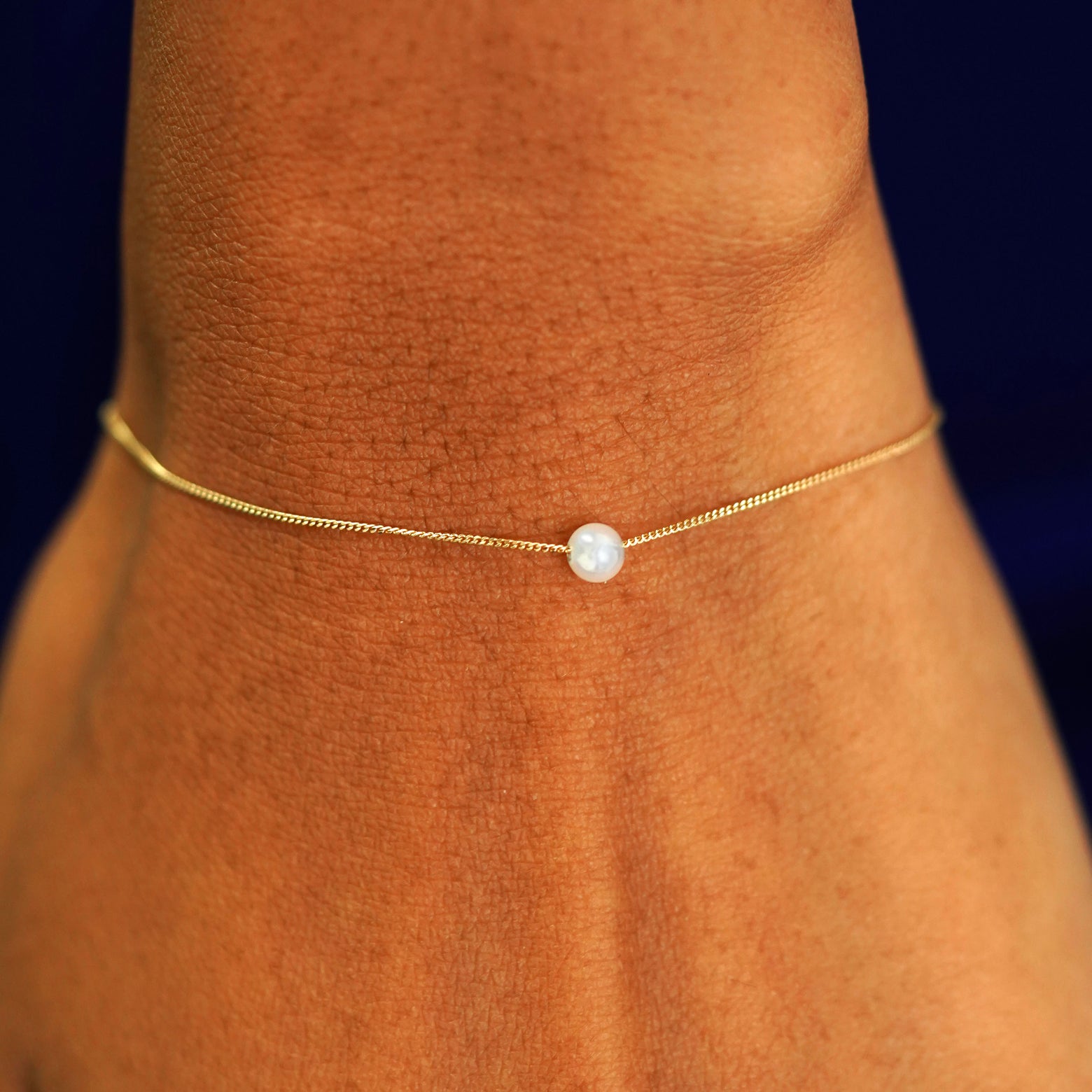 A model's wrist wearing a yellow gold Pearl Slide Bracelet with a 4mm pearl