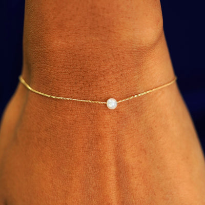 A model's wrist wearing a yellow gold Pearl Slide Bracelet with a 4mm pearl